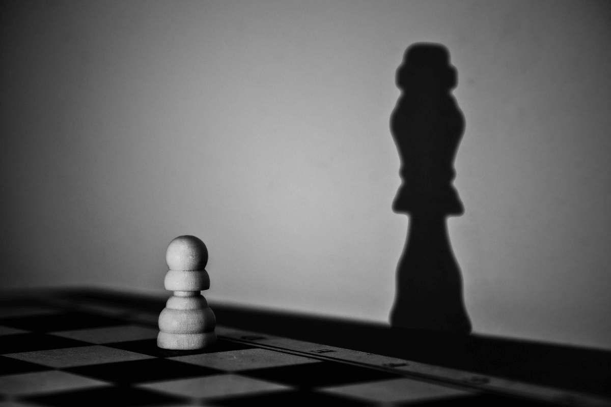 Ein Schachbauer wirft den Schatten einer König-Figur – ein Symbol für die unsichtbaren Team-Dynamiken und verborgenen Machtverhältnisse, die kulturelle Blockaden verursachen.